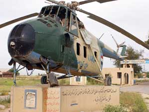 Driving their M1114 High-Mobility Multipurpose Wheeled Vehicle (HMMWV) past the remains of an Mil M-4 Hound display helicopter a convoy of US Air Force (USAF) and US Army (USA) personnel enter the main entrance of an abandoned helicopter Iraqi Air Base (AB) to perform a site-survey during Operation IRAQI FREEDOM.