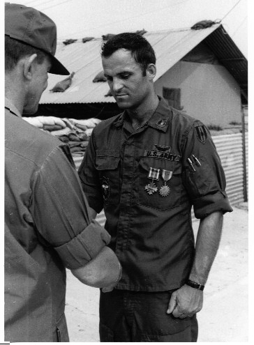 The author standing beside a facsimile of their unit patch outside their orderly room on 7 Mar 70, after being promoted to unit commander at Red Beach in Da Nang. (Photo courtesy of the author.)